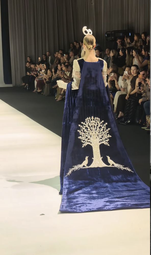 A Tree of Life in silver crystal with two birds across the train of a Prussian-blue velvet gown