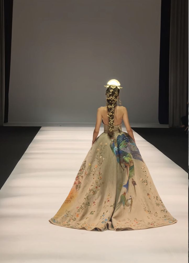 A full-skirted gown seen from behind, a Persian garden of peacocks and foliage painted across the skirt