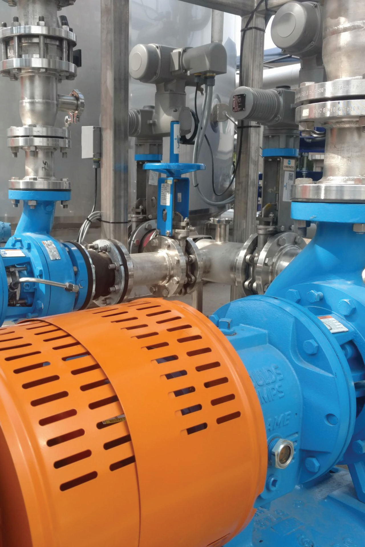 Close-up of a blue industrial pump with an orange cover and connected metal pipes with valves.