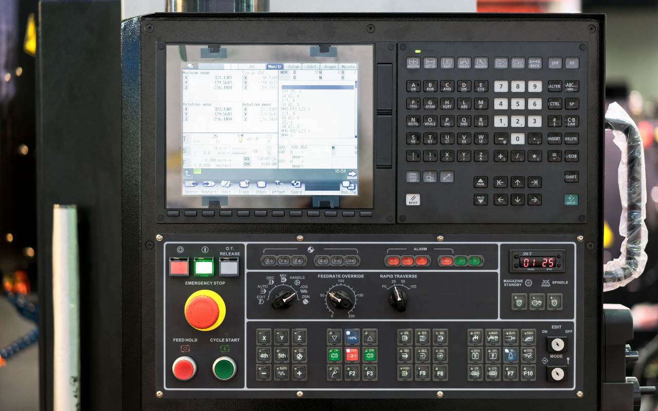 Control panel of an industrial CNC machine with screen, buttons, switches, and emergency stop button.