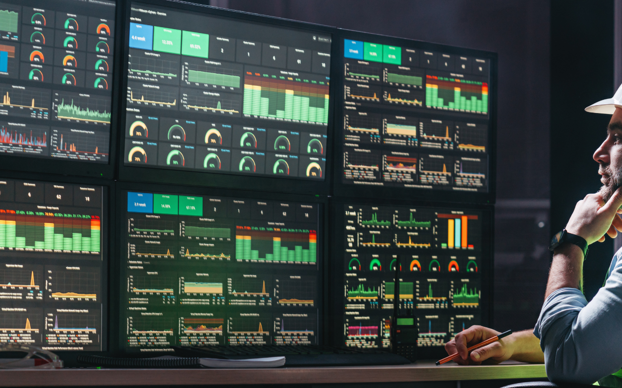 Man in white helmet analyzing performance dashboards with charts and graphs on multiple monitors.