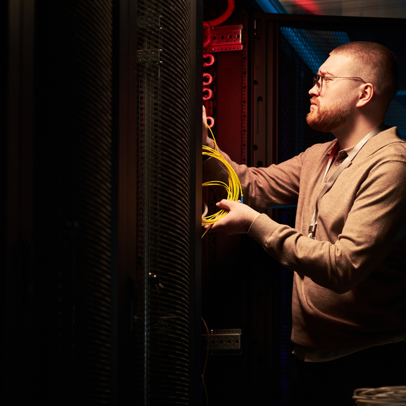 Technician holding yellow network cables working inside a dark server rack cabinet.