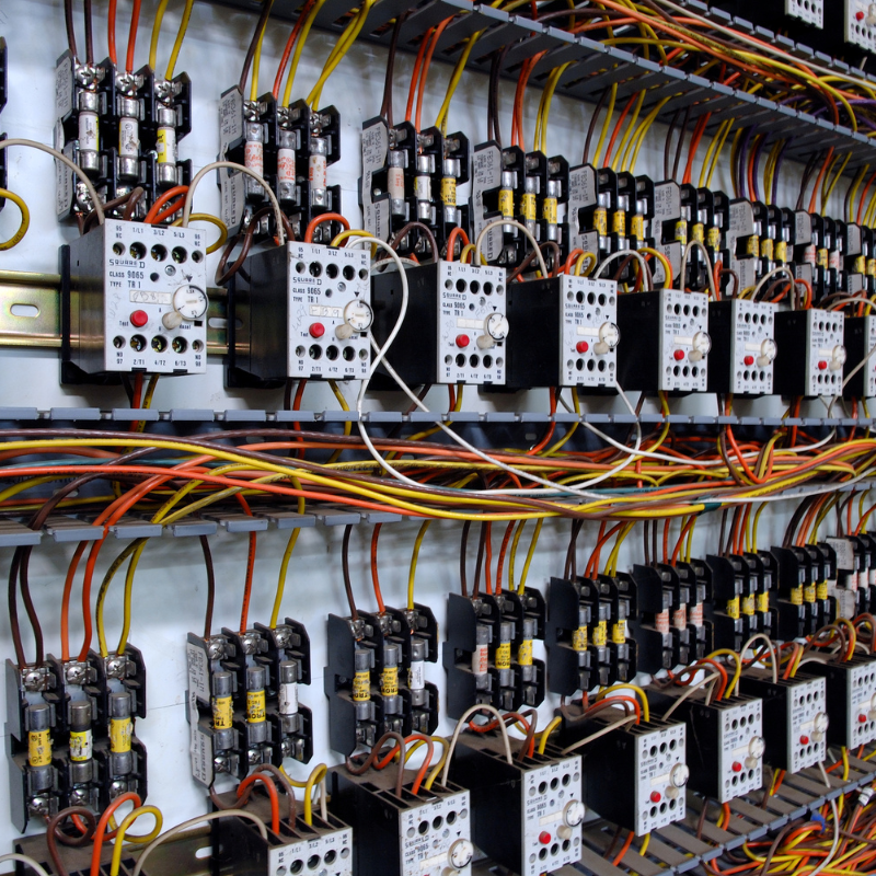 Rows of electrical relays and circuit breakers with colorful wiring inside an electrical panel.