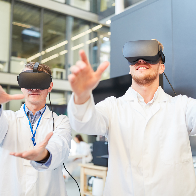 Two men in lab coats using virtual reality headsets and reaching out with their hands indoors.