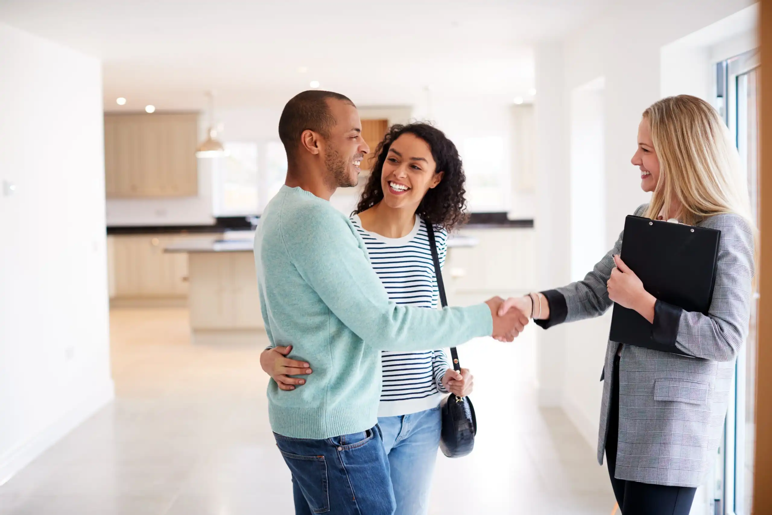 Homebuyers shaking hands with a real estate agent inside a home.