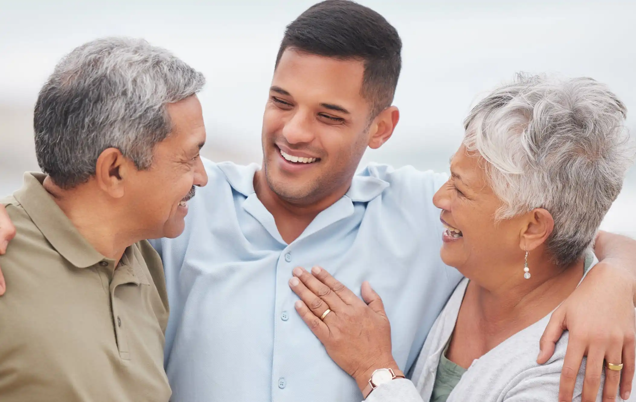 A smiling younger man embracing an older man and woman.