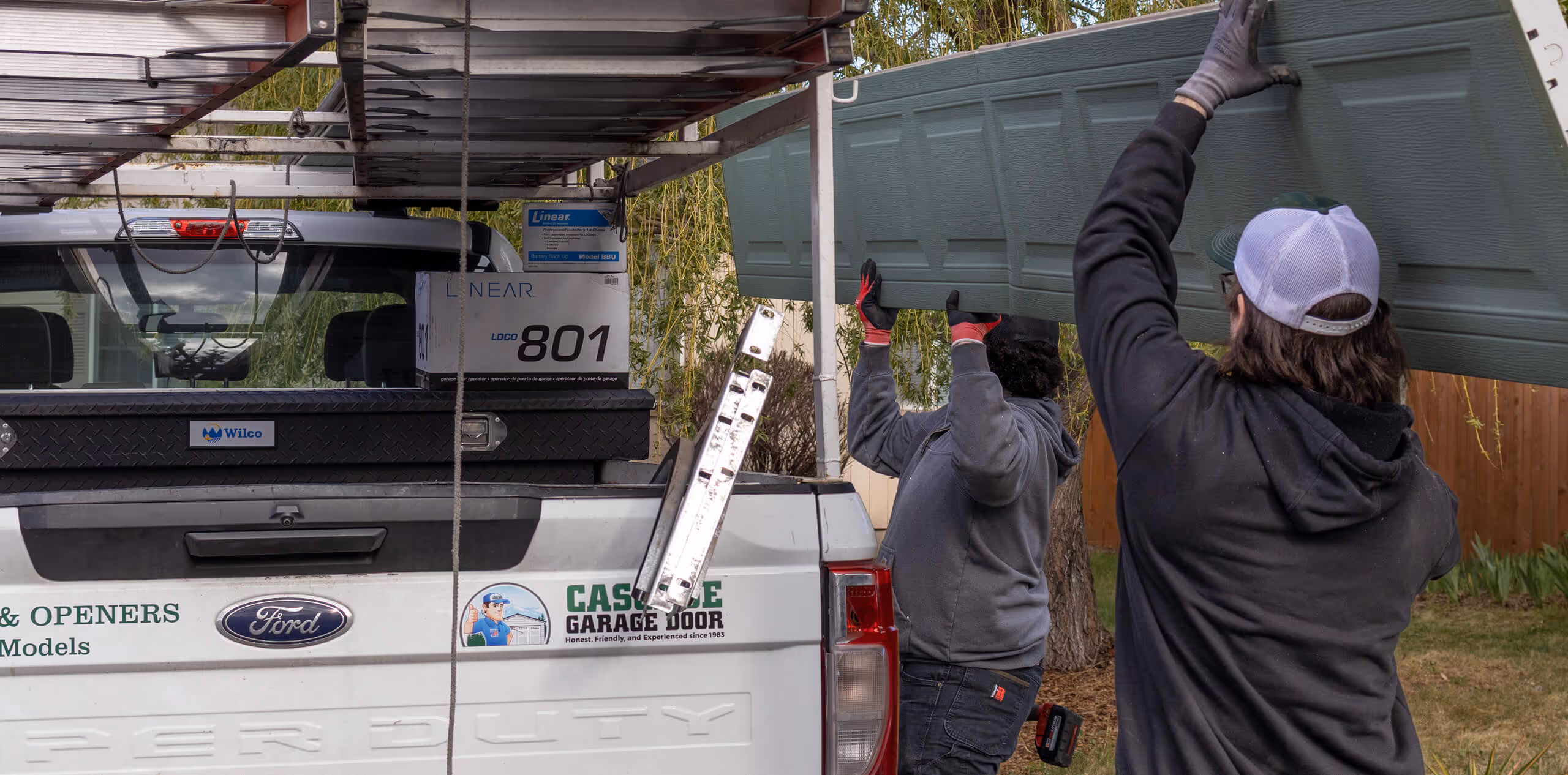 Two garage door technicians loading an old garage door panel onto a utility truck