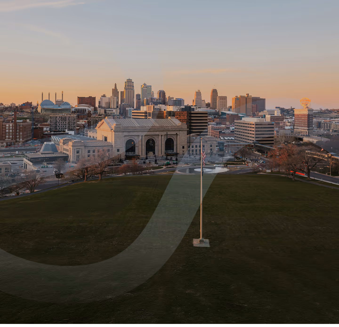 Kansas City skyline at sunset with Union Station and a flagpole in the foreground.