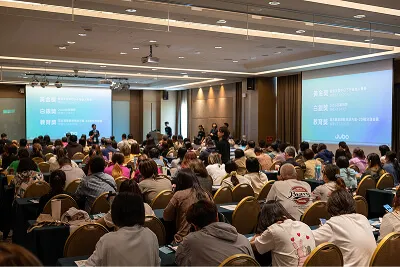 一場室內研討會，眾多聽眾面對兩個大型投影屏幕和演講者。