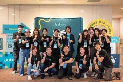 Group of people posing and smiling at an event booth with Jubo branding in the background.