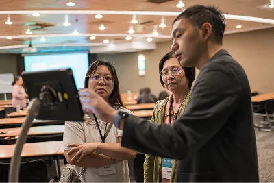 Three adults in a classroom discuss content on a tablet device.