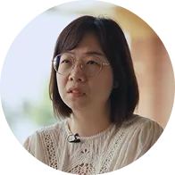 一位佩戴圓形眼鏡、短髮，穿白色蕾絲上衣的女性正注視前方。
