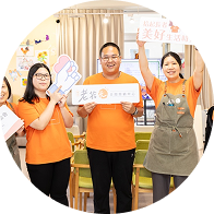 Three people smiling and holding signs in a bright room with posters and a thermometer chart.