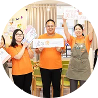 Three people smiling and holding signs in a bright room with posters and a thermometer chart.