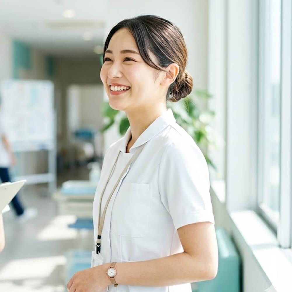 穿白色護士服、微笑並側身站立在明亮醫療環境中的年輕女性護士。