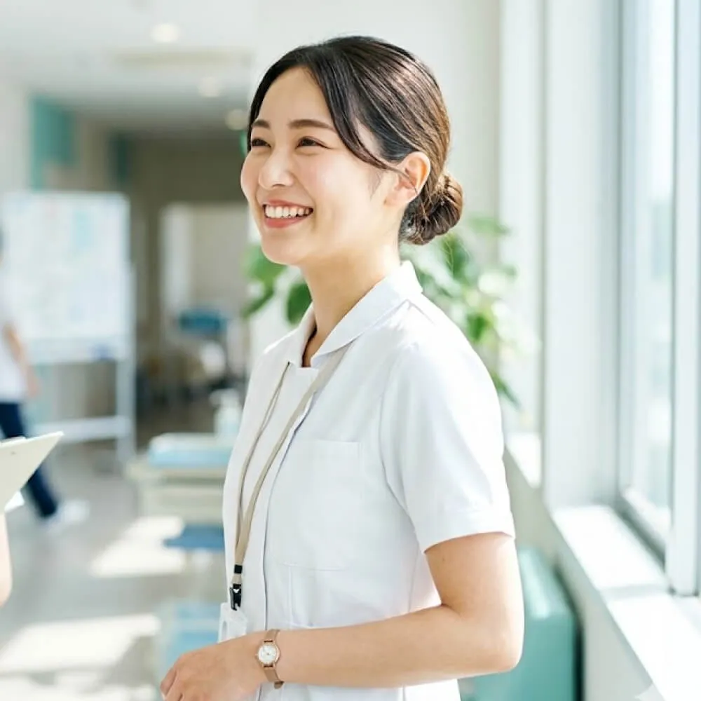 穿白色護士服、微笑並側身站立在明亮醫療環境中的年輕女性護士。