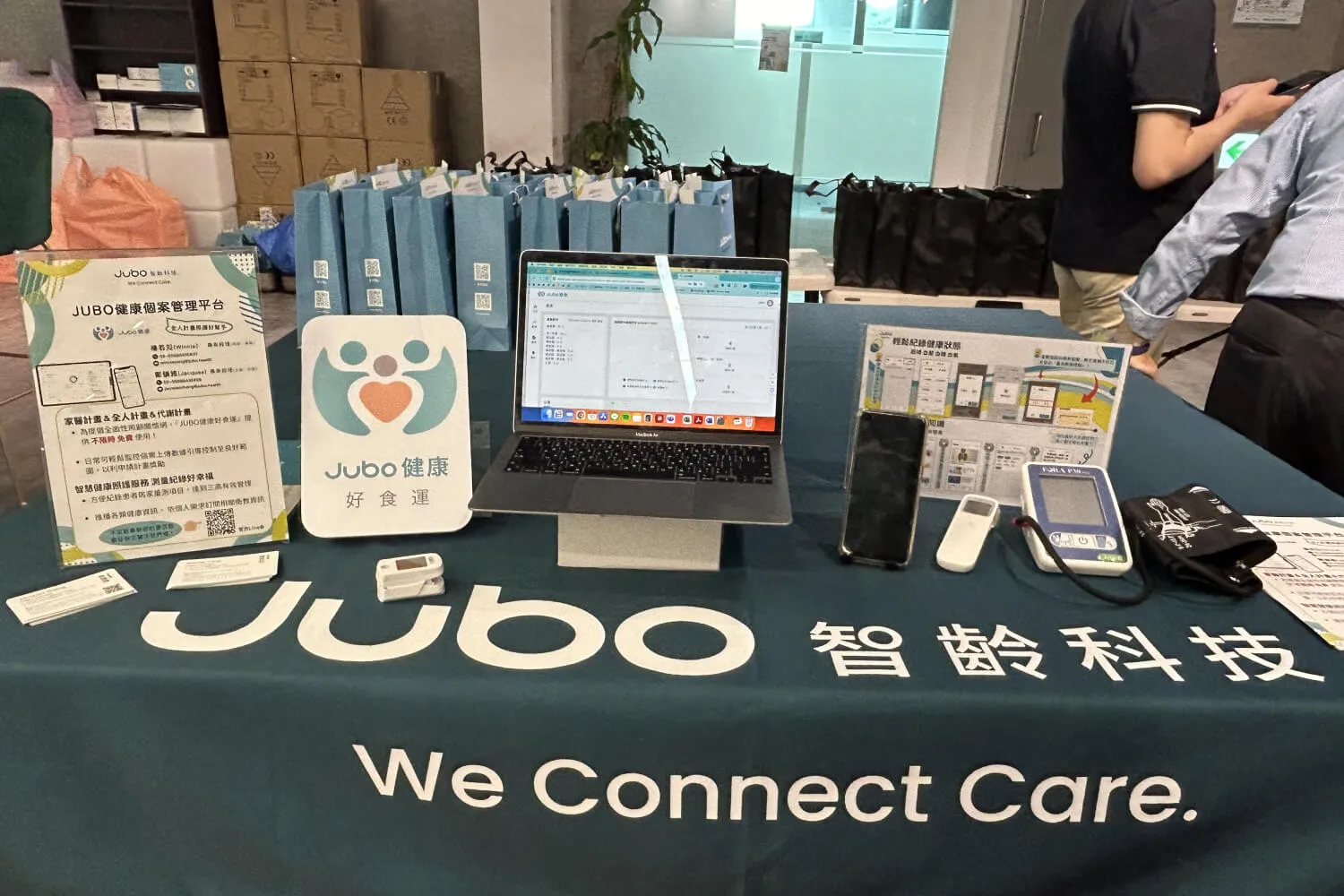 展示桌上有Jubo健康個案管理平台宣傳資料、筆記型電腦和健康監測設備。