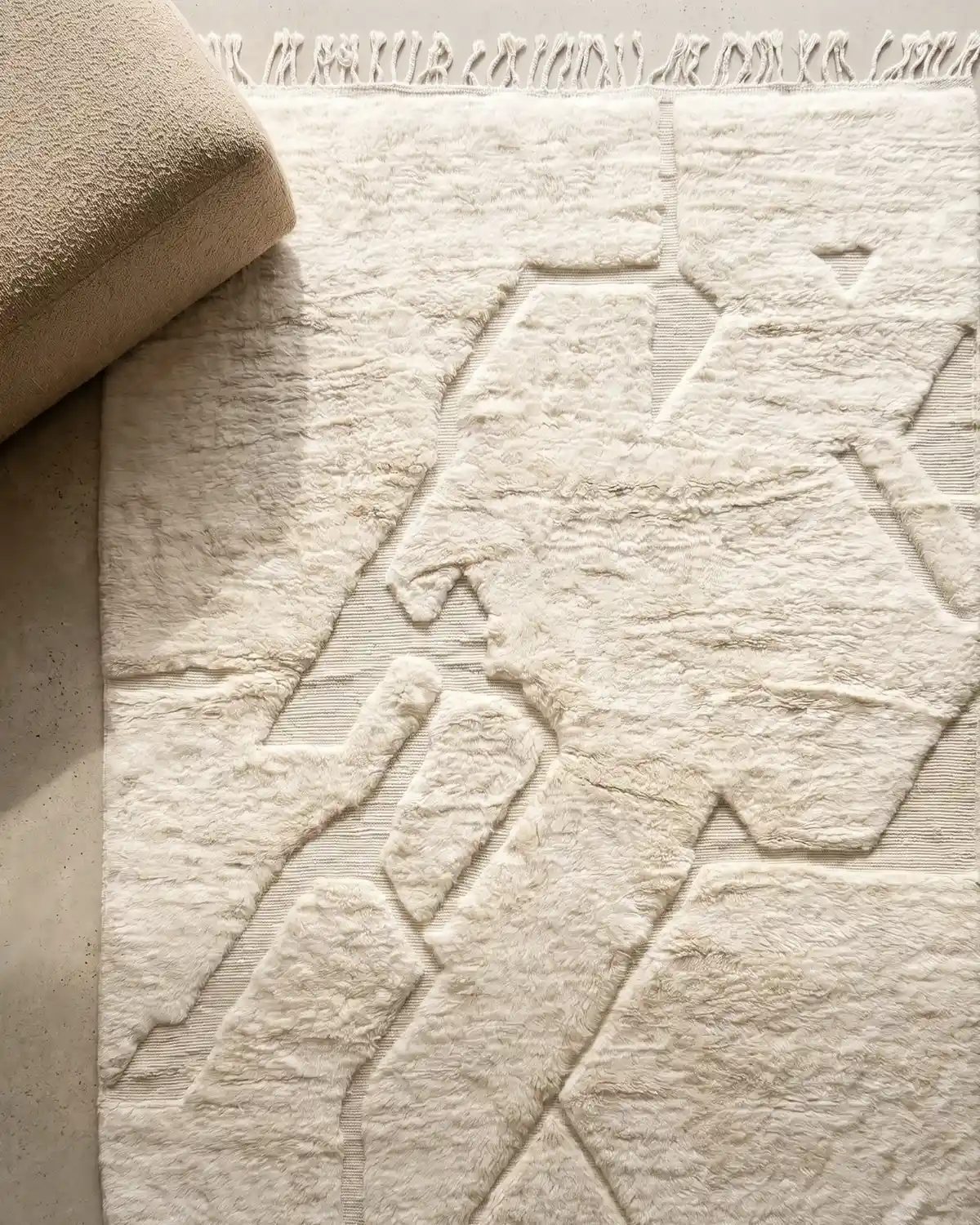 Coco handwoven rug detail – overhead close-up of abstract organic relief pattern in natural ivory wool with twisted fringe