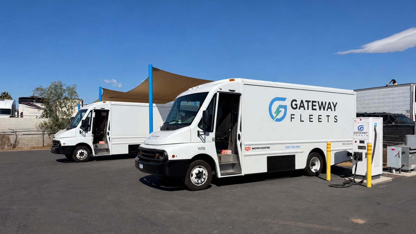 Two white Gateway Fleets electric delivery trucks parked at a charging depot, with a Workhorse W56 connected to a charger.