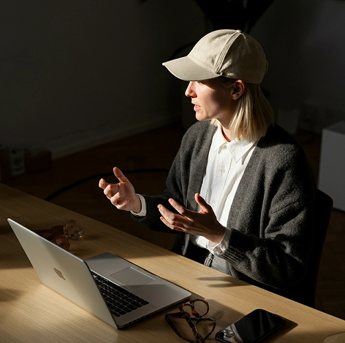 Woman in a cap explaining ideas at a desk with a laptop in dramatic side light