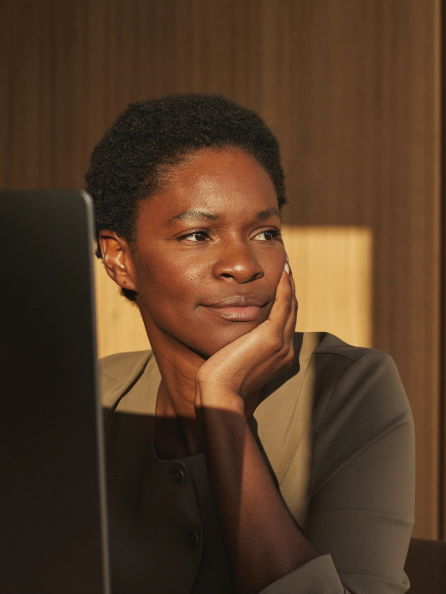 A professional Black woman sitting in front of a laptop resting her head on her hand in a warm lit office