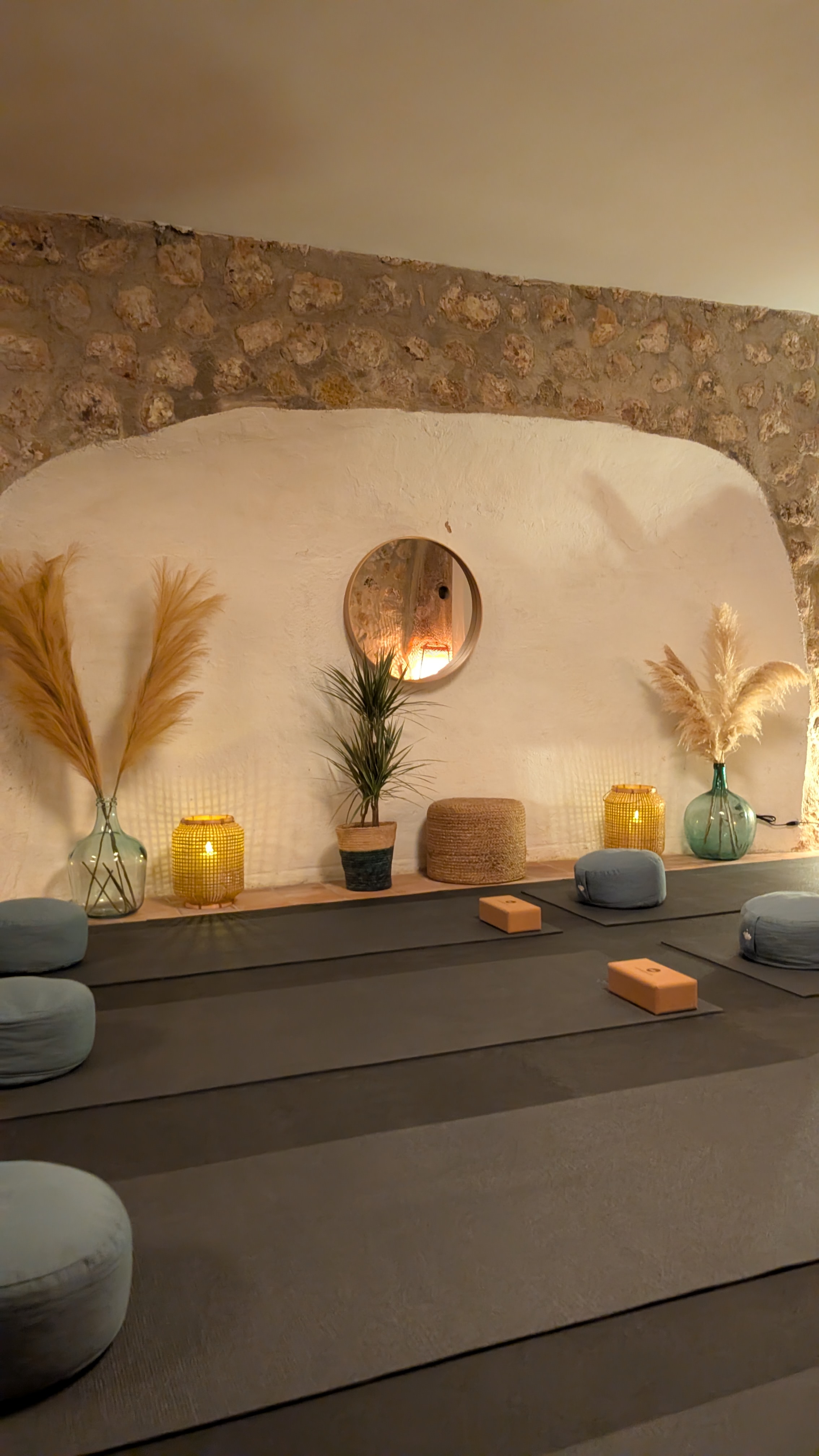 Yoga mats and wooden blocks neatly lined up in parallel for a large group, set in a bright yoga shala with lush plants.