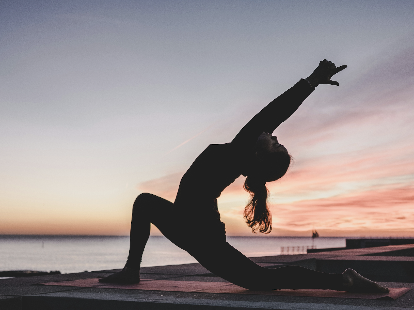 Silhouette of a person performing a yoga stretch on a mat at sunset by the sea.