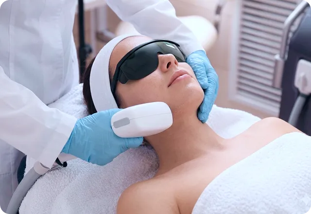 Woman wearing protective goggles receiving a laser dermatology treatment on her chin from a gloved practitioner.