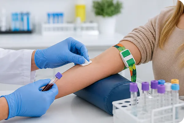 Gloved hands drawing blood from arm with tourniquet, test tubes and lab setting visible.