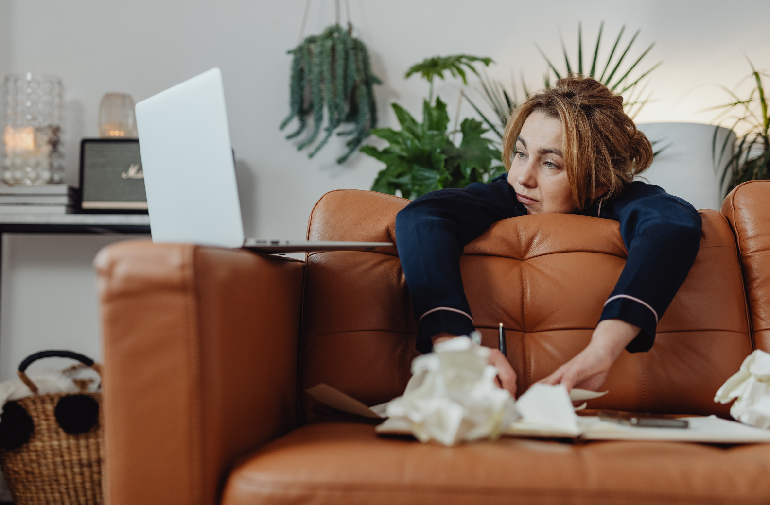 Woman in her pajamas leaning over coach looking despondent.