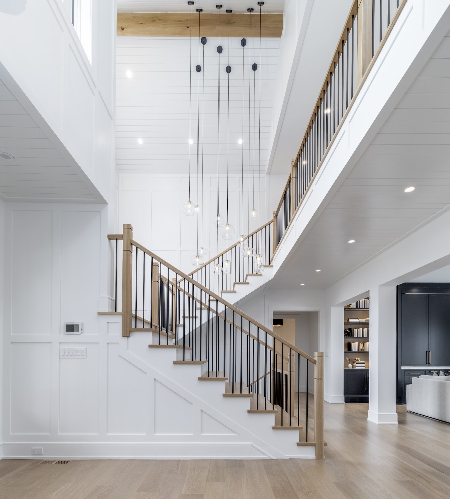 Two-story staircase hall with white oak and black iron staircase and cascading glass globe pendants in a Lloyd Harbor new-build.