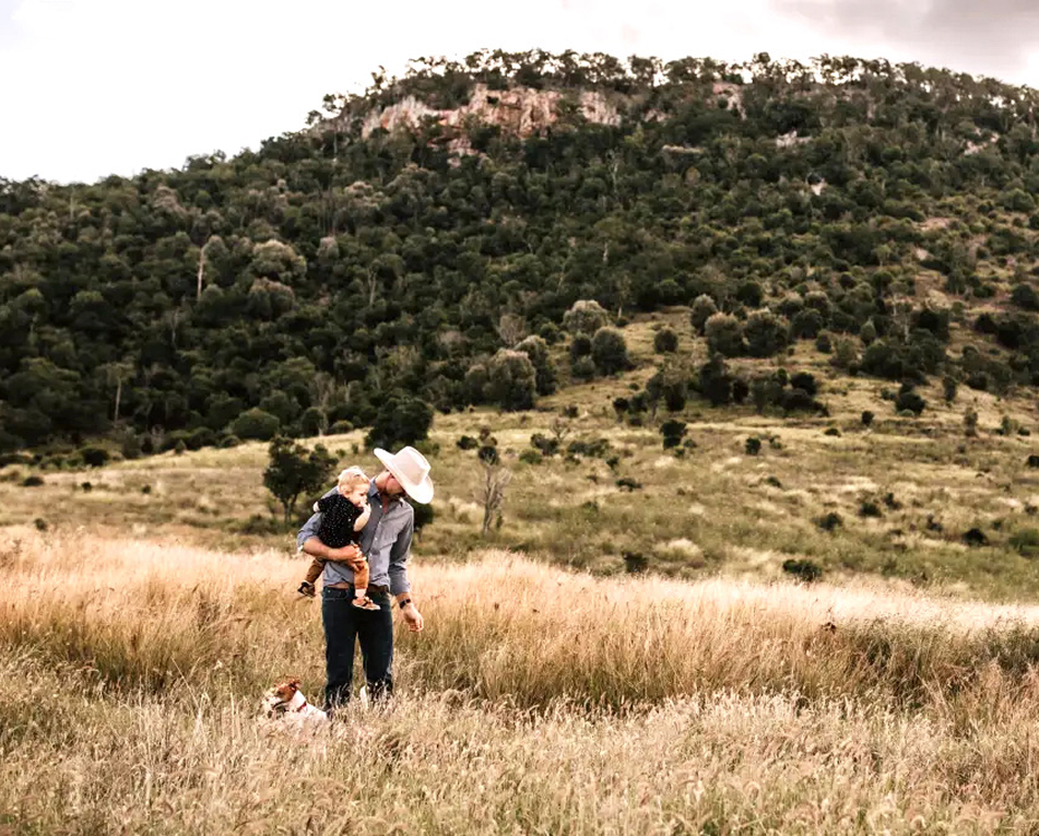 The owner of Tarramba walks through a pasture holding his child