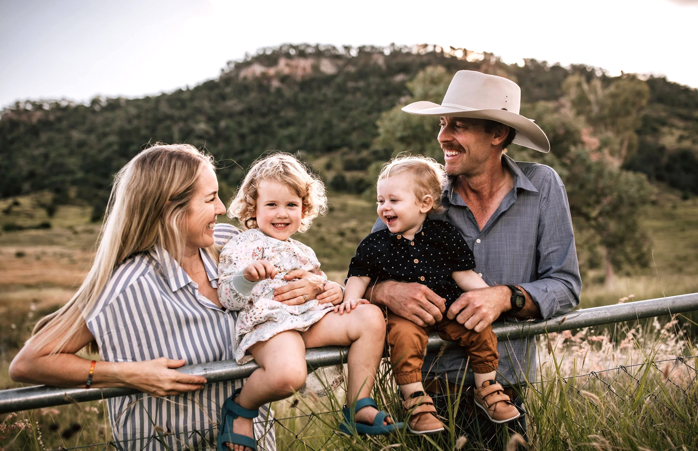 Adam, his wife and children lean on a fence in a field