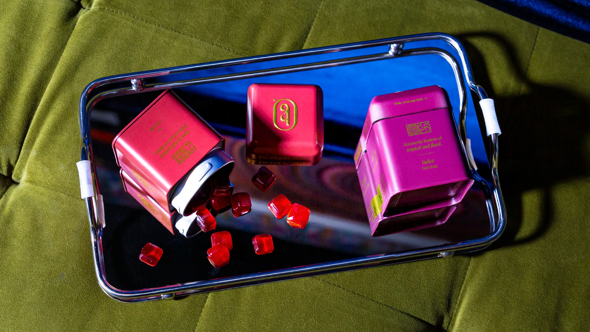 Three magenta Boxer Six tins on a chrome tray with red diamond-cut gummies