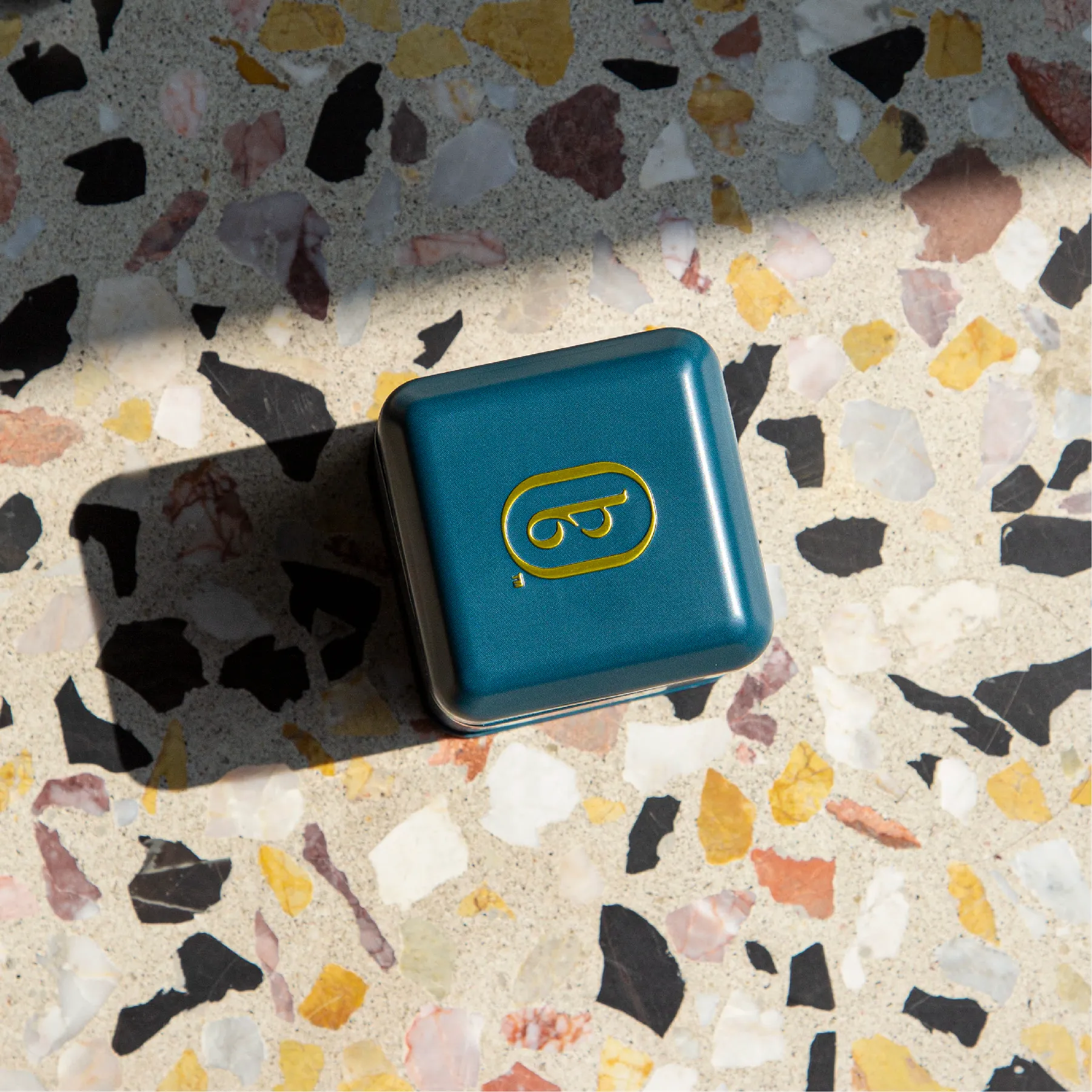 Overhead view of a teal Boxer Six tin lid on terrazzo