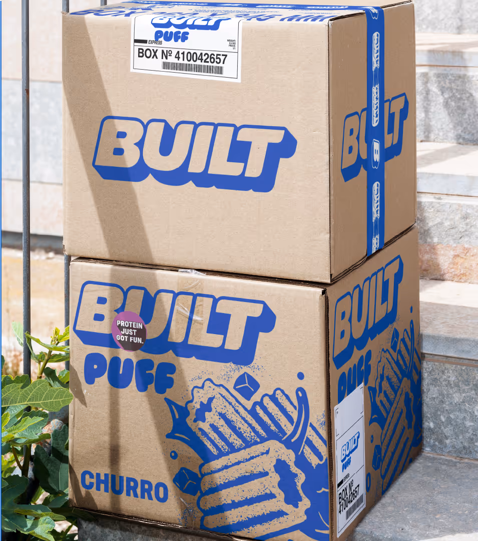 Two cardboard shipping cartons printed with blue Built and Built Puff Churro logos on a concrete step.