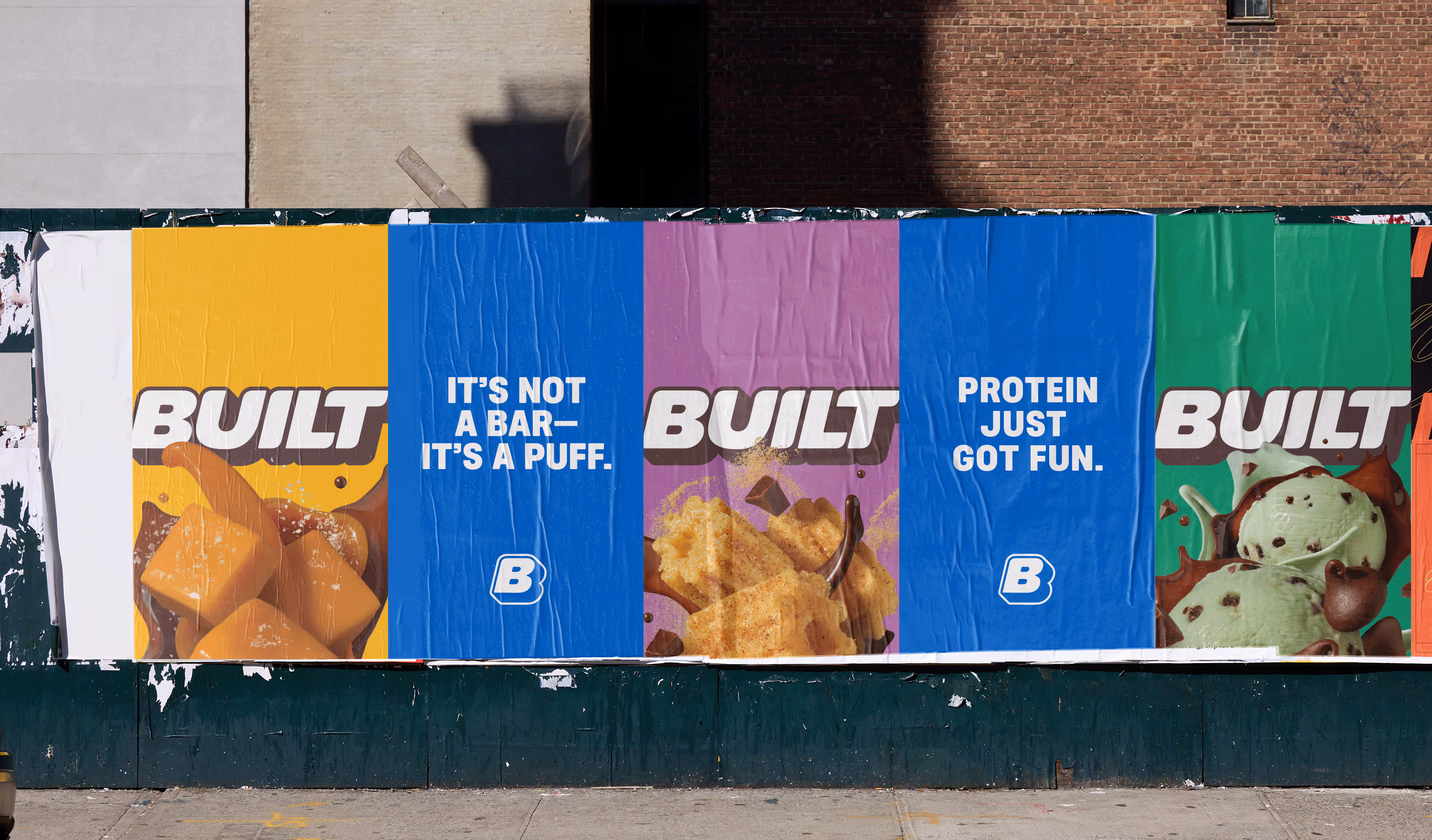 Row of yellow, blue, purple, and green Built posters wheatpasted on a brick city wall.