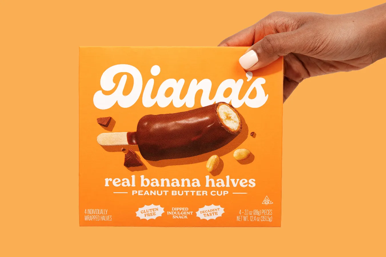 Hand with white nails holding an orange Diana's Peanut Butter Cup box on matching orange.