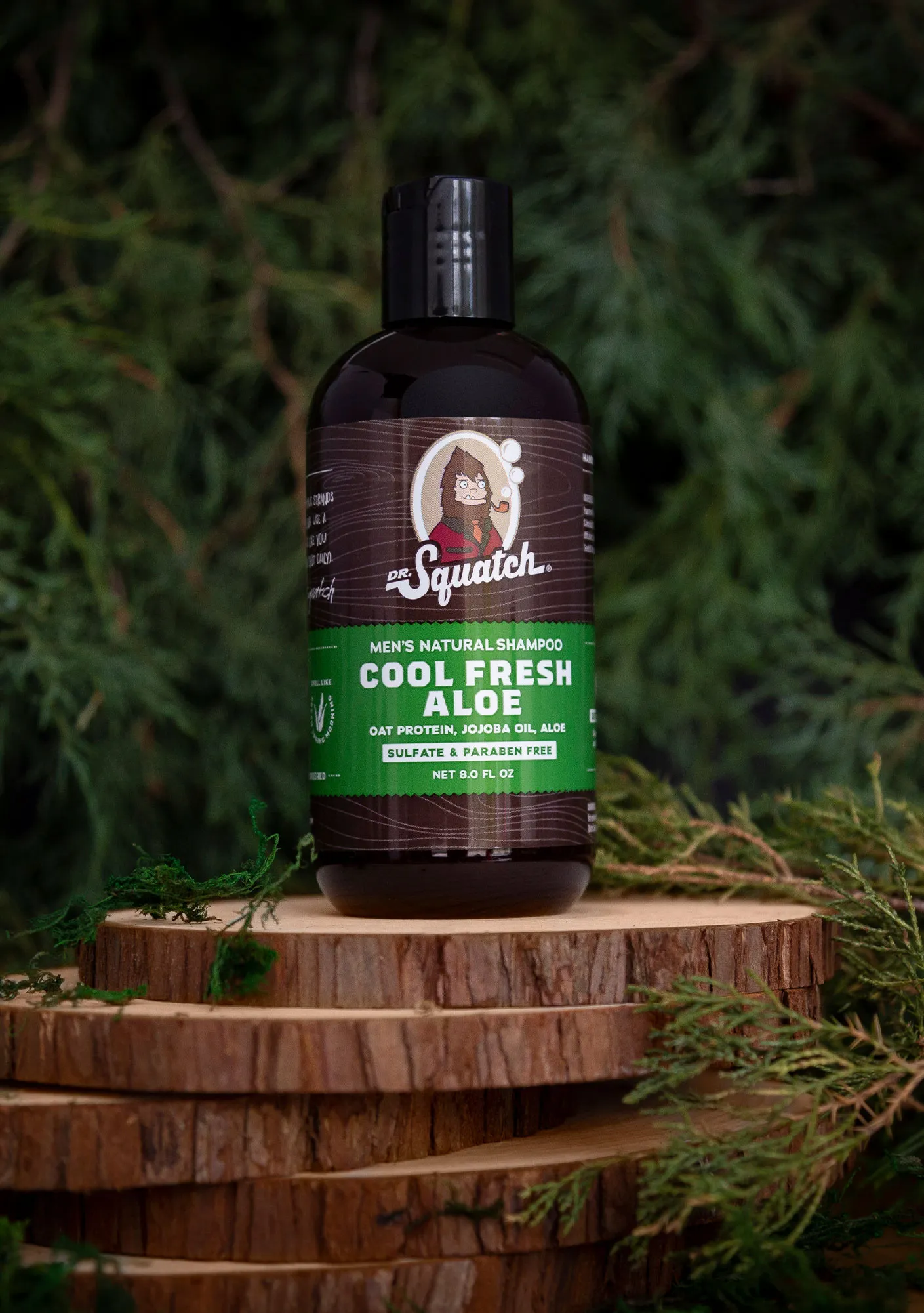 Dr. Squatch Cool Fresh Aloe shampoo bottle on stacked wood slices with cedar foliage.