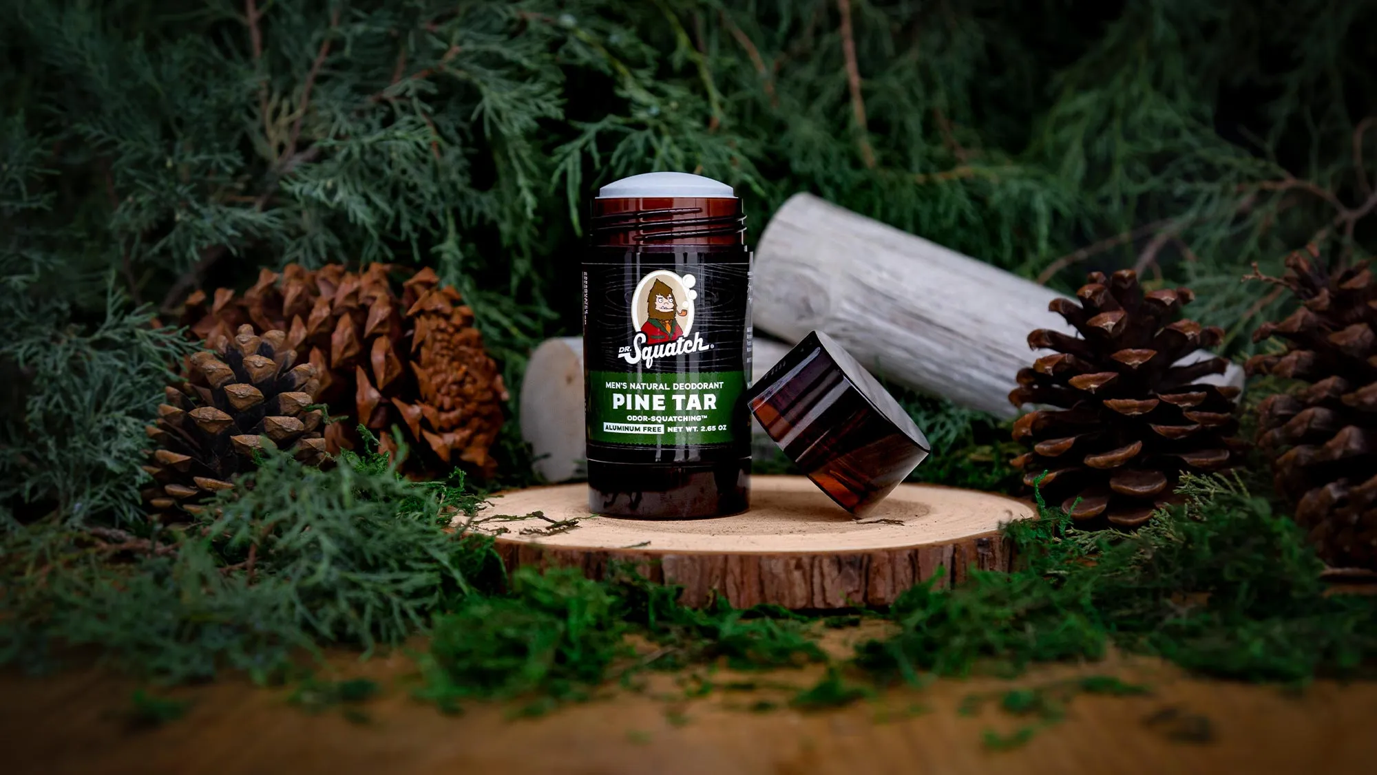 Uncapped Dr. Squatch Pine Tar deodorant on a wood slice with moss and pine cones.