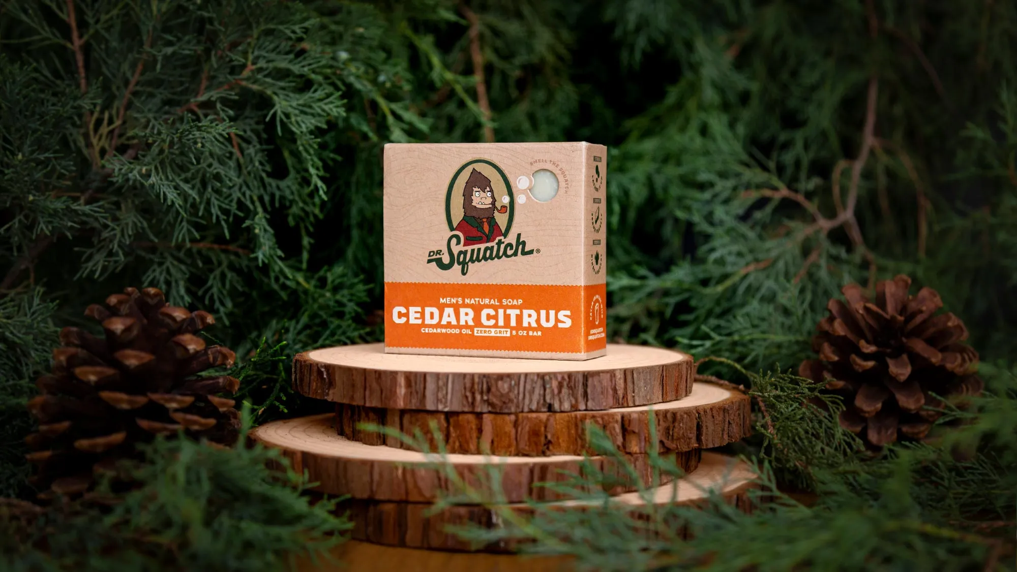 Cedar Citrus Dr. Squatch soap box on stacked wood slices with cedar branches and pine cones.