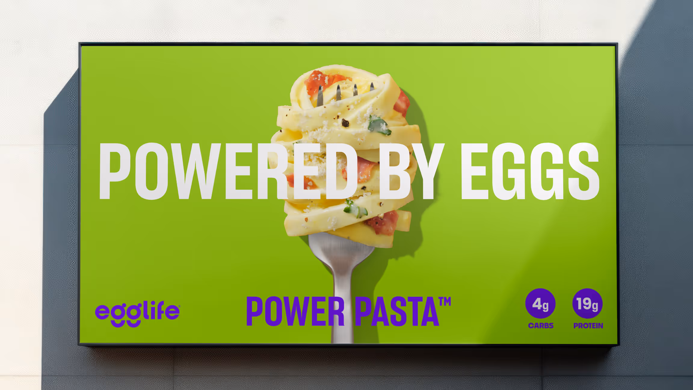 Outdoor green billboard reading 'Powered by eggs' with a forkful of pasta and 4g carbs / 19g protein callouts.