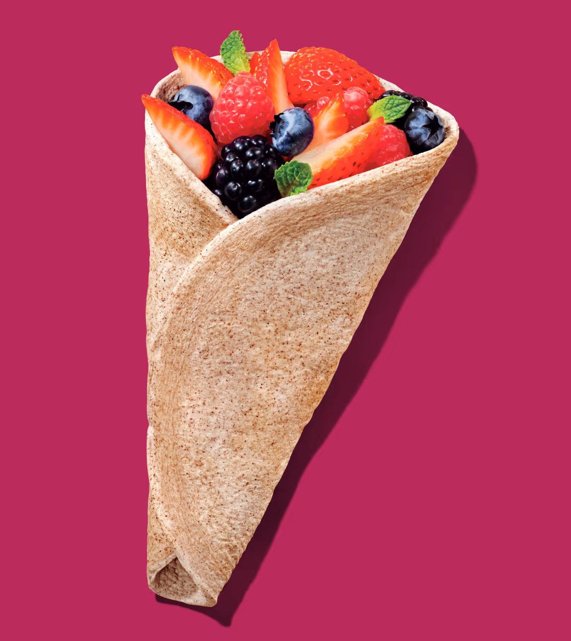 Tan egg-white wrap filled with strawberries, blackberries, blueberries, and mint on a magenta background.