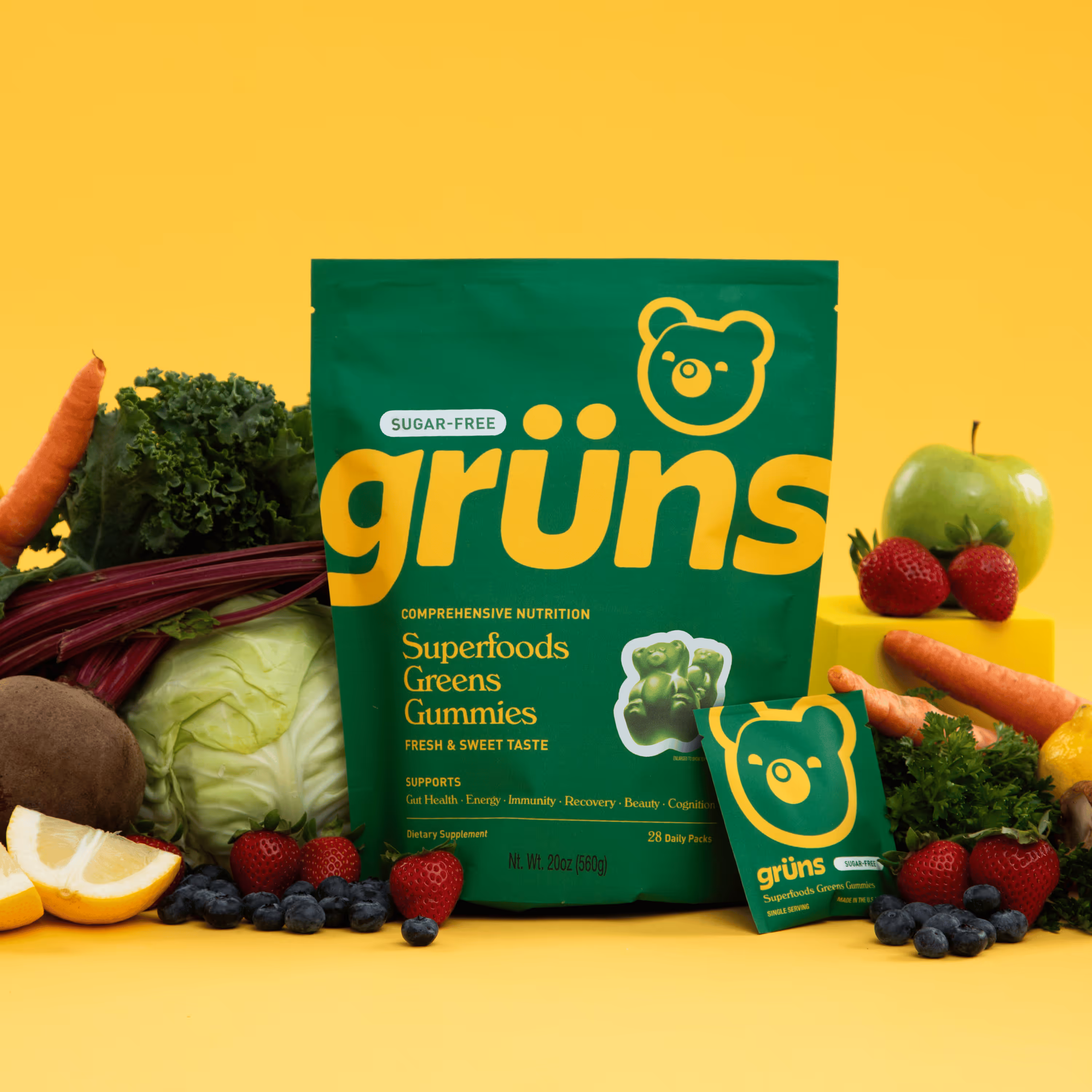 Green Grüns Greens Gummies pouch surrounded by carrots, kale, beets, kiwi, lemon, strawberries, and parsley.
