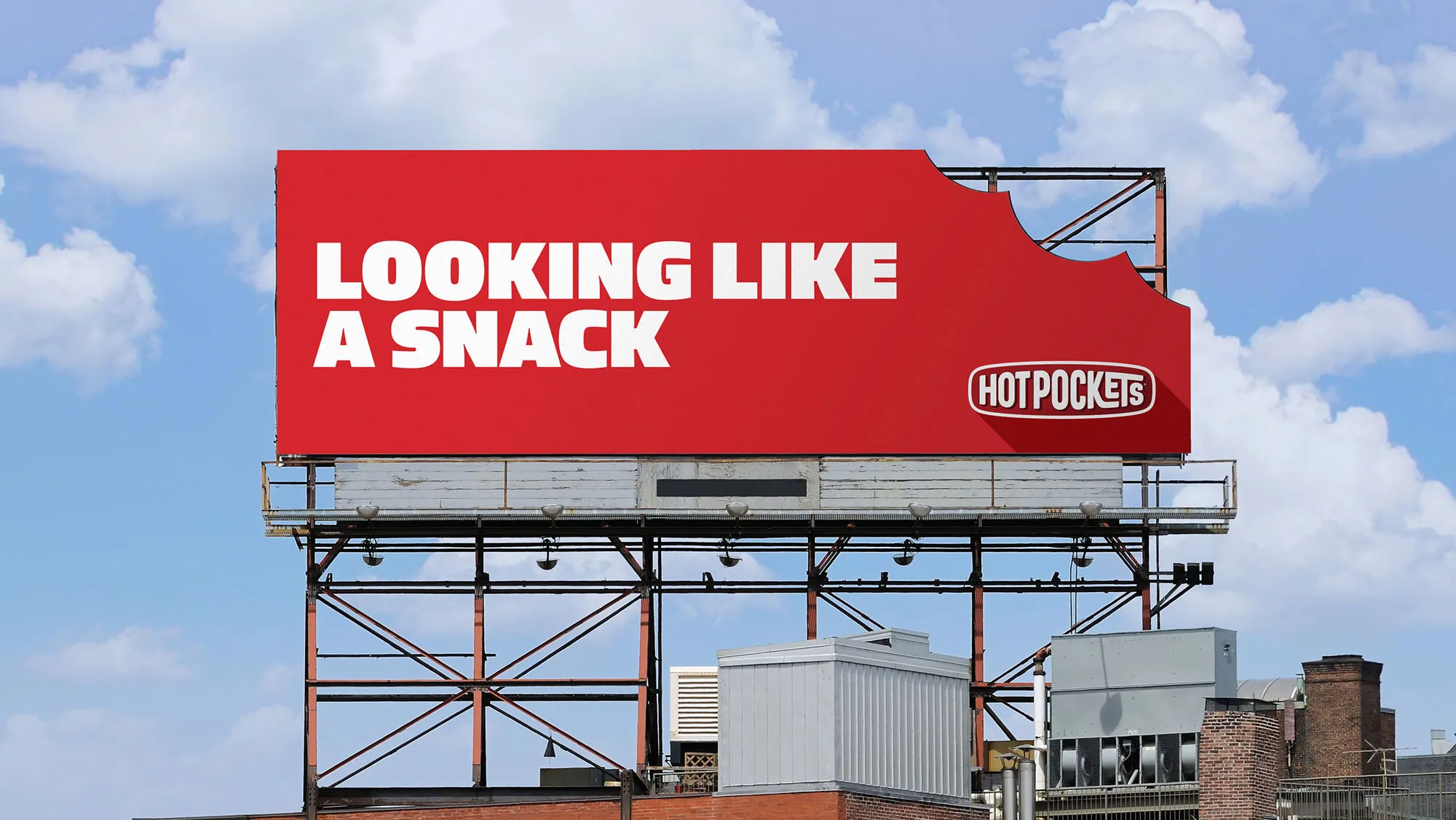 Outdoor billboard against cloudy sky reading 'Looking like a snack' with a bite-corner Hot Pockets logo.