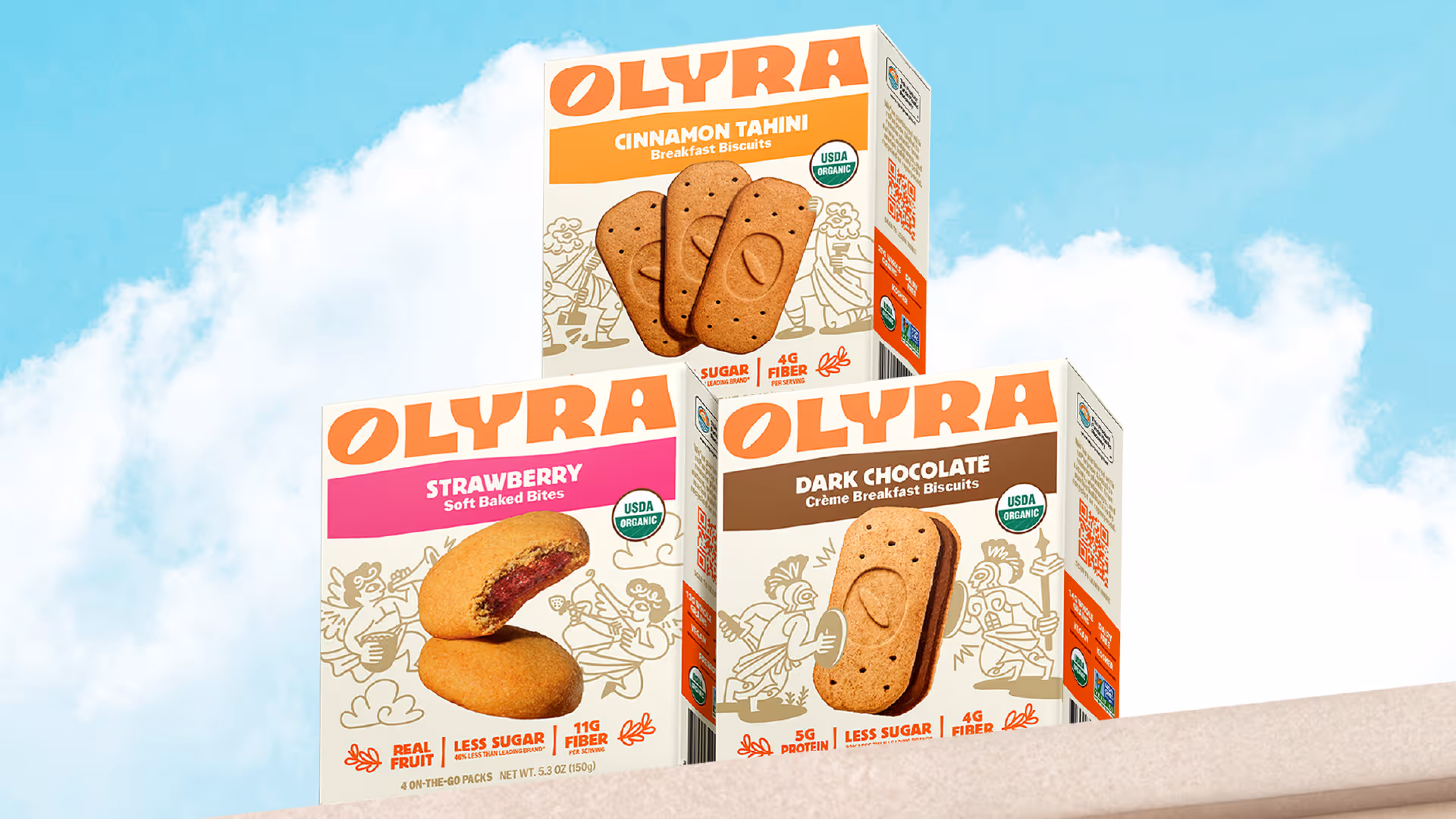 Three Olyra packages against blue sky: Cinnamon Tahini Biscuits, Strawberry Soft Baked Bites, Dark Chocolate Creme Biscuits.