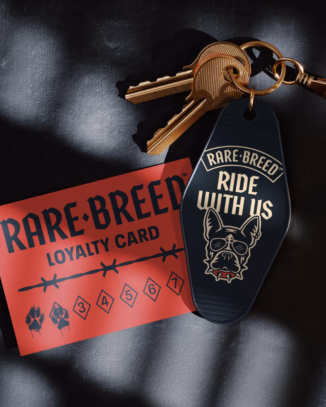Red Rare Breed loyalty card with paw-print punches beside a black 'Ride with us' keychain fob and brass keys.