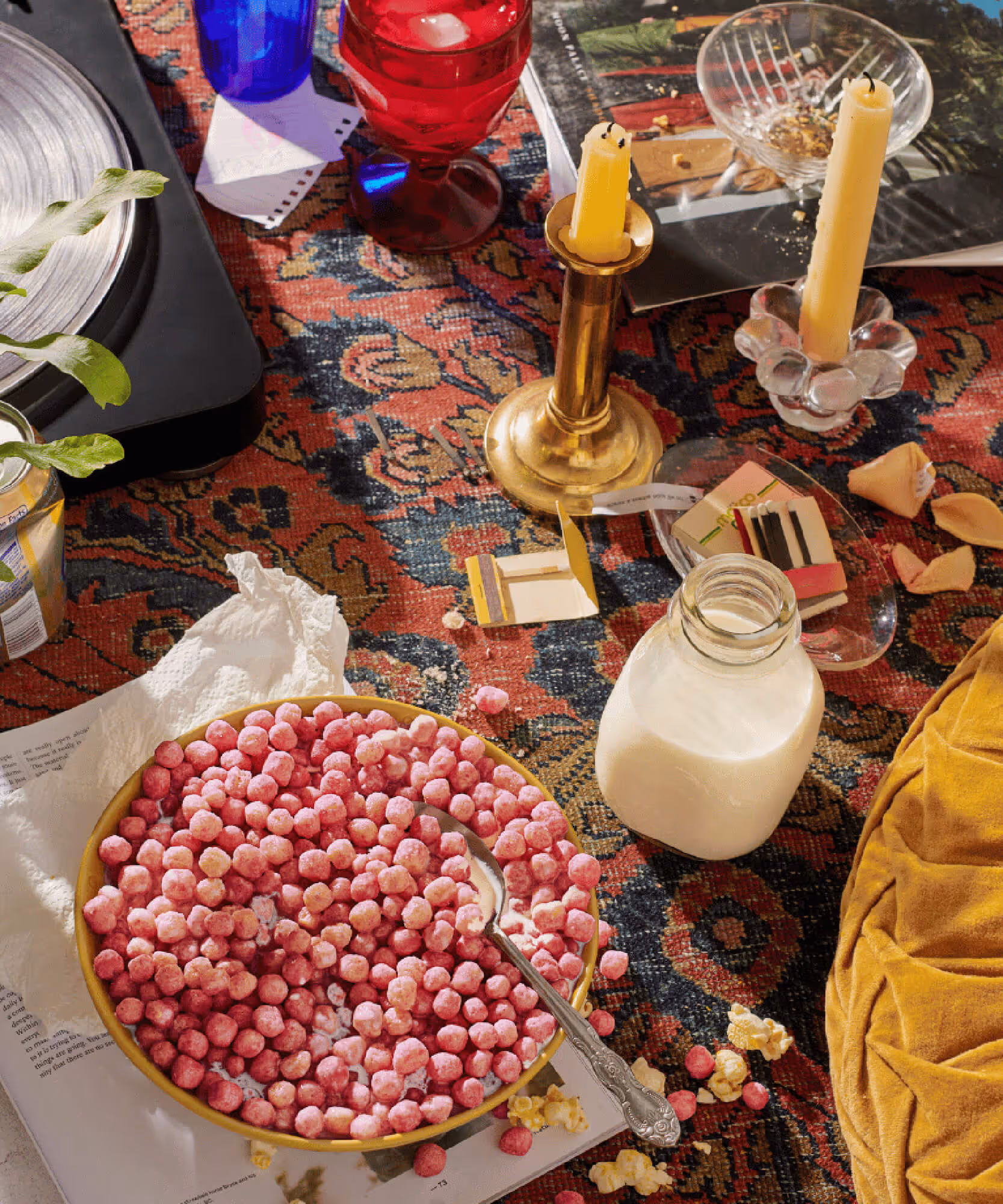 Pink cereal puffs in a white bowl sit on a patterned tablecloth with a lit candle, flowers, and colorful glasses.