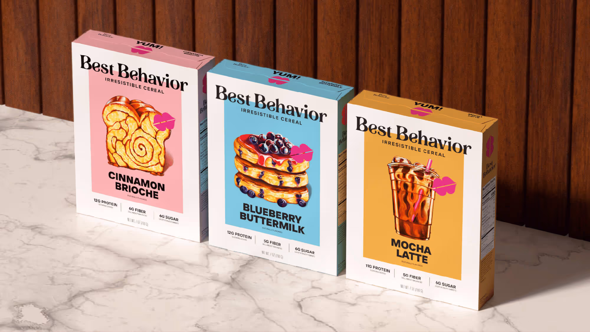 Three Best Behavior cereal boxes — Cinnamon Brioche, Blueberry Buttermilk, and Mocha Latte — on a marble surface.
