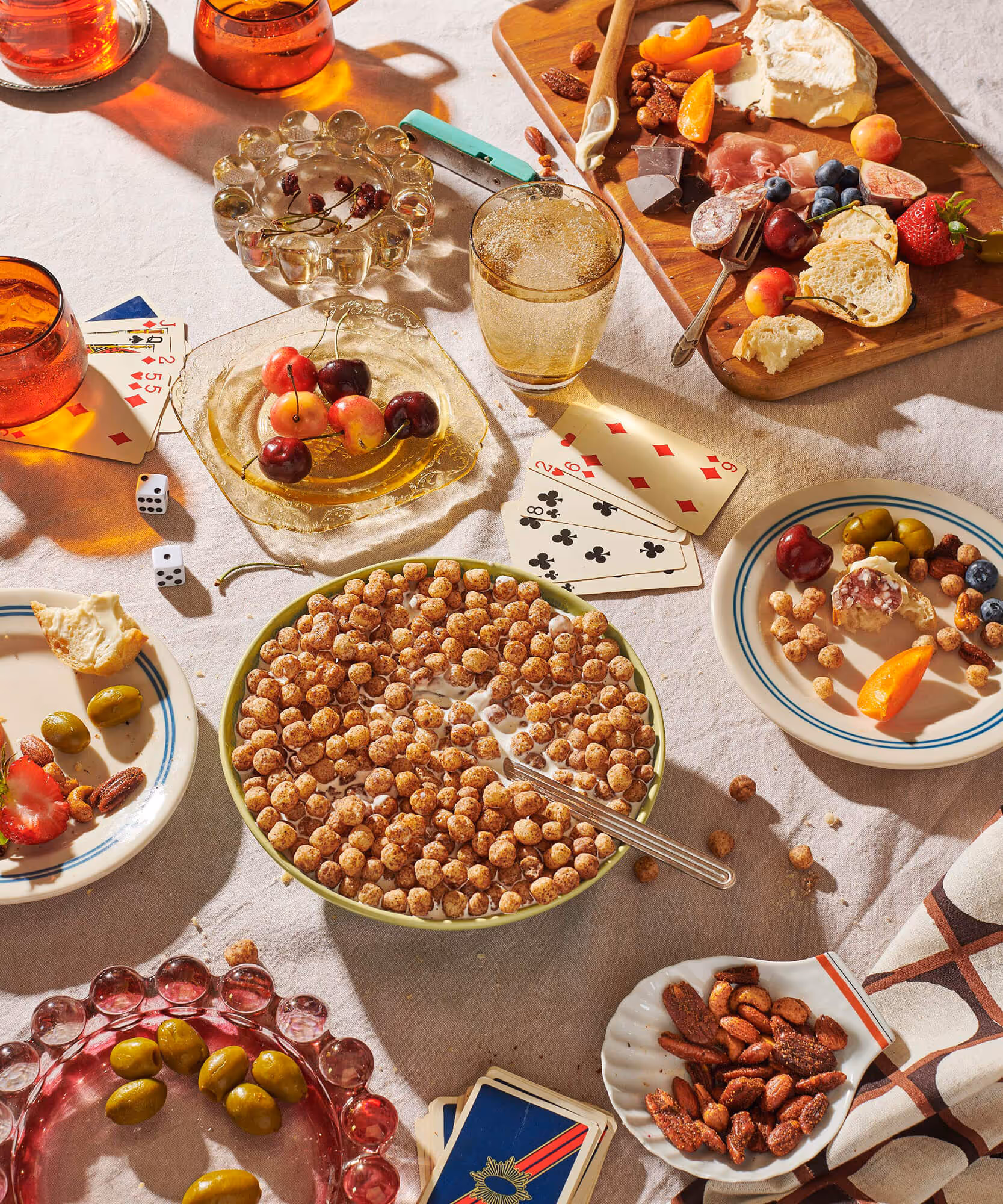 Overhead view of a party spread with bowls of cereal, charcuterie, drinks, and snacks on a table.